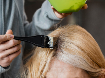 Colorist brushing grey root coverage onto blonde hair