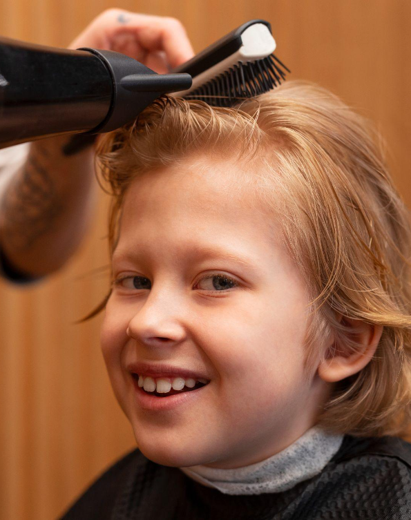 Smiling child getting a blow-dry with a round brush at a children’s hair salon after a gentle kids haircut