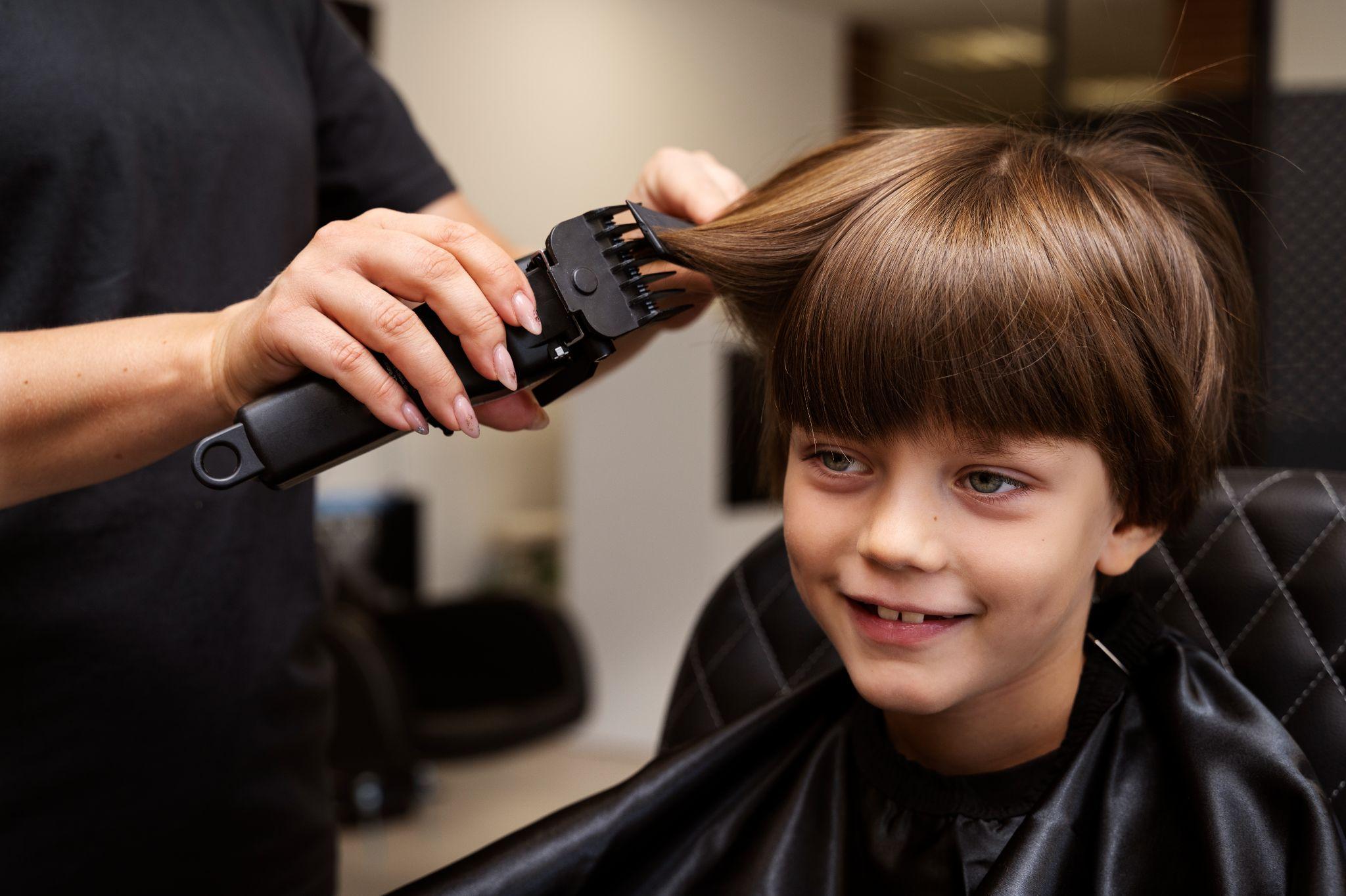 Boy having bangs trimmed with clipper-comb at a kid-friendly barbershop, neat school-ready kids haircut.