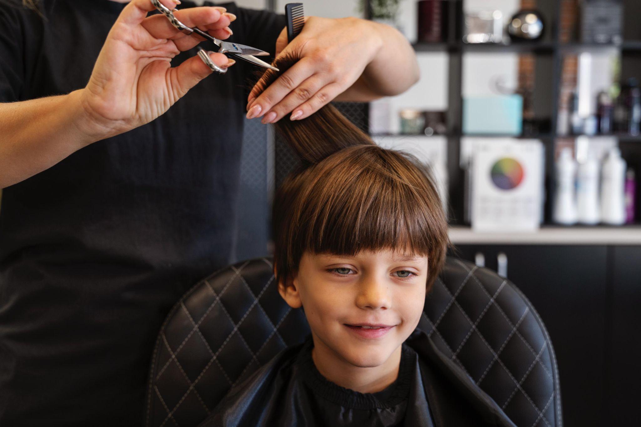 Stylist cutting a boy’s hair with scissors and a comb, a precise kids haircut at a family hair salon