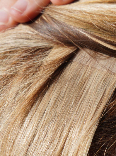 Close-up of tape-in hair extension bonded to blonde natural hair section.