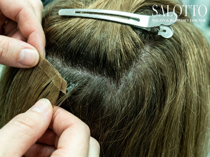 Stylist carefully removes tape-in extensions during Salotto Salon refresh appointment.